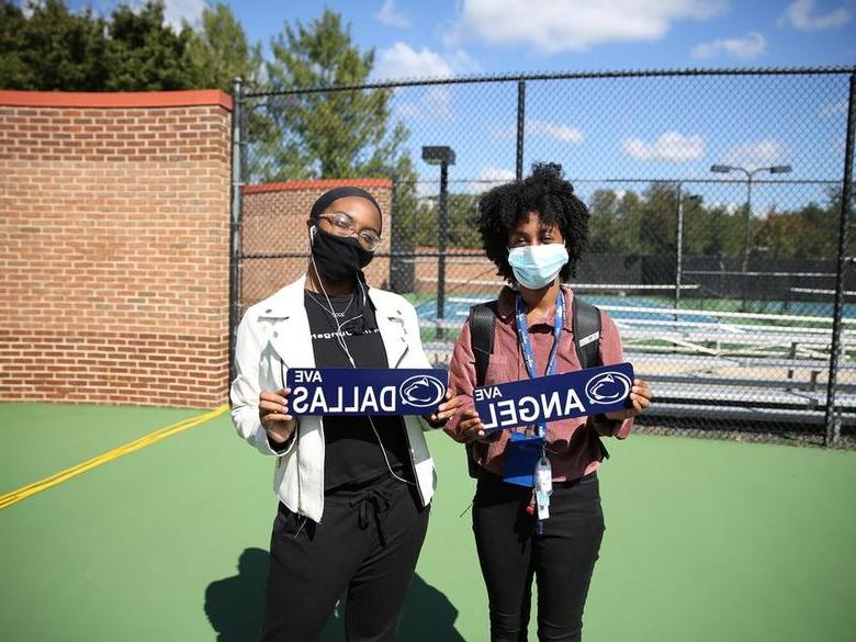 两名女学生戴着口罩，举着写有自己名字的牌子.
